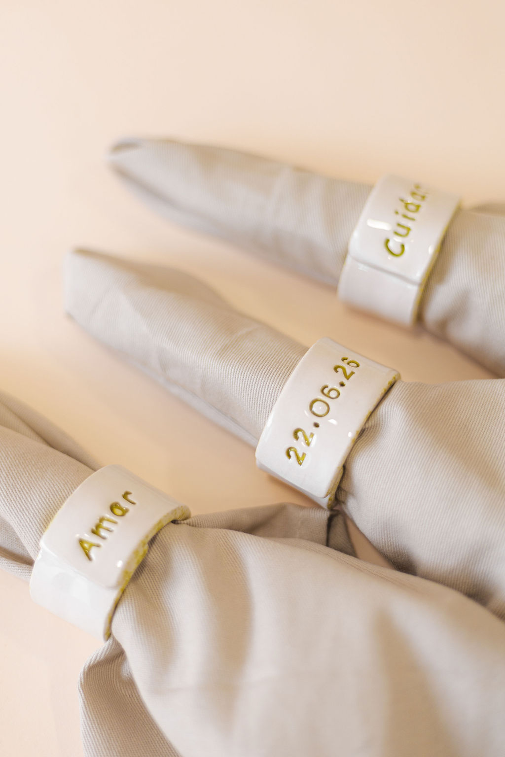 Anéis de guardanapo brancos em cerâmica com texto dourado em guardanapos bege