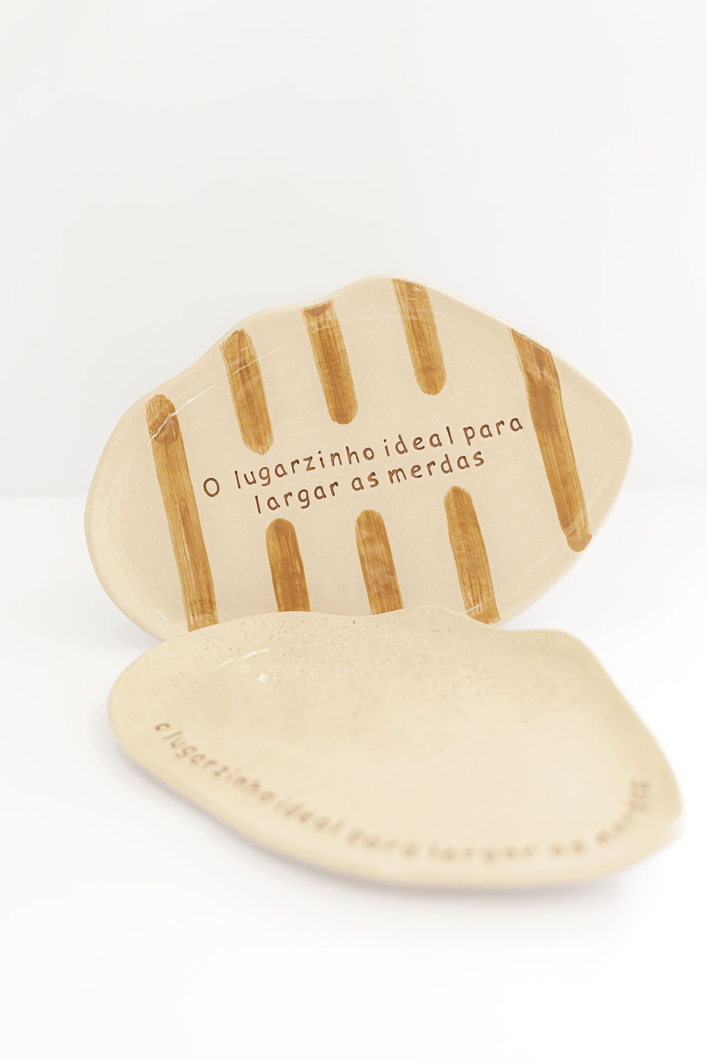 Duas peças de cerâmica bege, uma com riscas castanhas e texto, a outra lisa e com texto, sobre fundo branco.