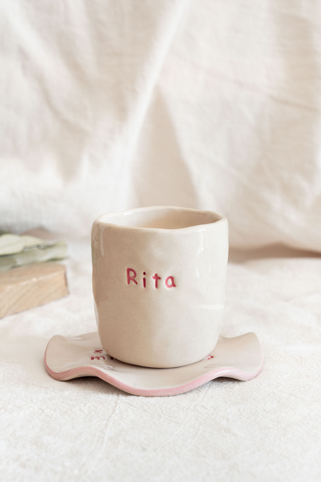 Caneca cerâmica branca com o nome Rita em relevo cor-de-rosa, em base ondulada branca com bordas cor-de-rosa