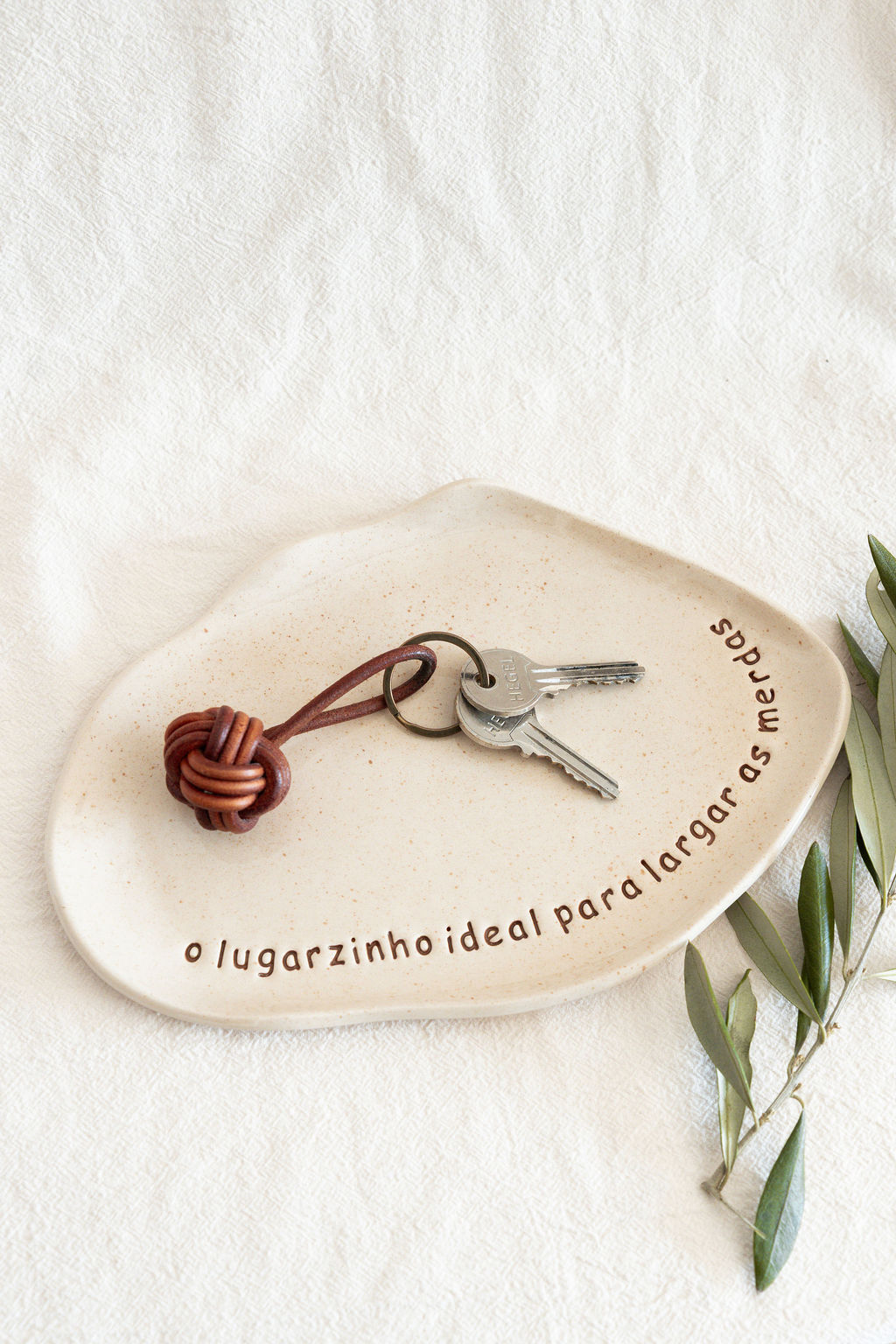 Prato decorativo de cerâmica bege com texto e chaves sobre tecido branco com ramo de folhas
