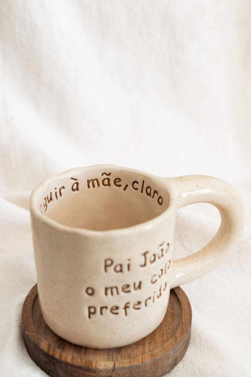 Caneca cerâmica bege com texto em castanho e suporte de madeira redondo