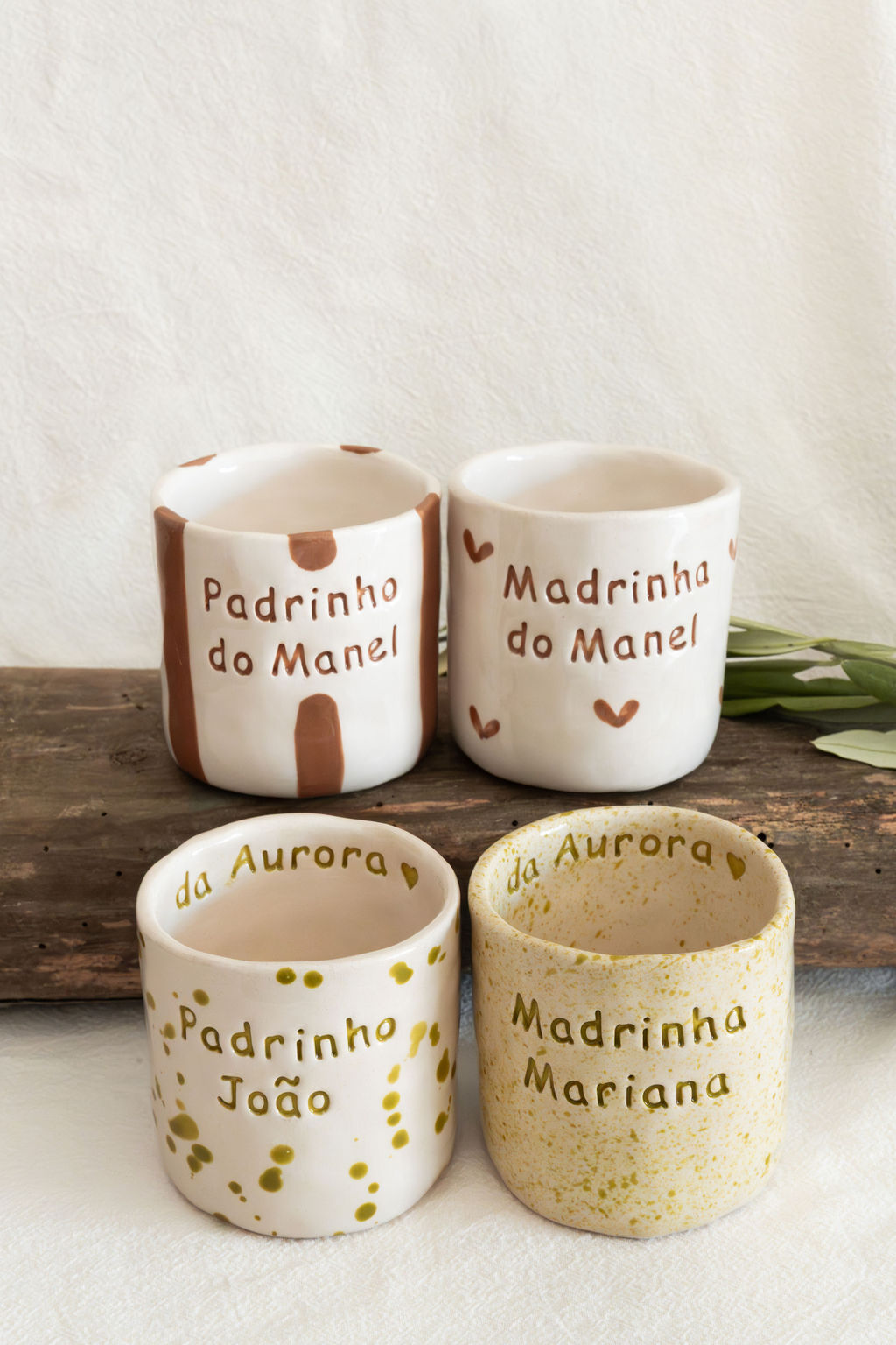Quatro canecas de cerâmica com textos personalizados e padrões manchados, sobre superfície de madeira.