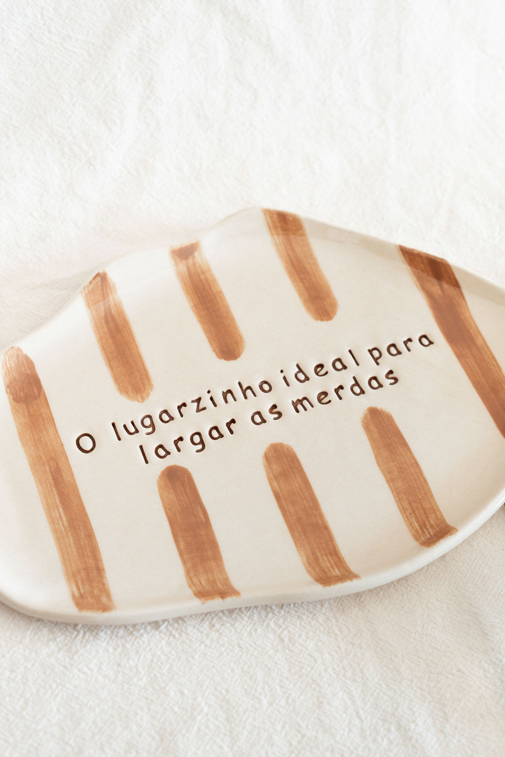 Prato em cerâmica com riscas castanhas e texto gravado em português