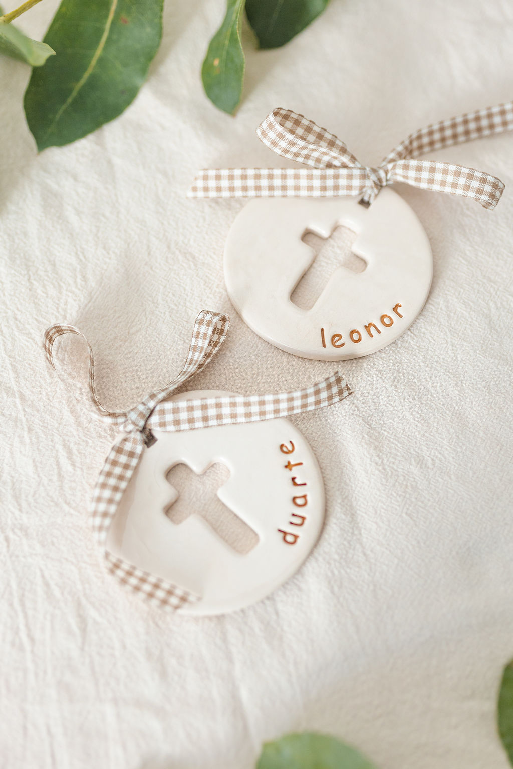 Decorações de cerâmica branca com recorte de cruz e nomes personalizados com fitas xadrez