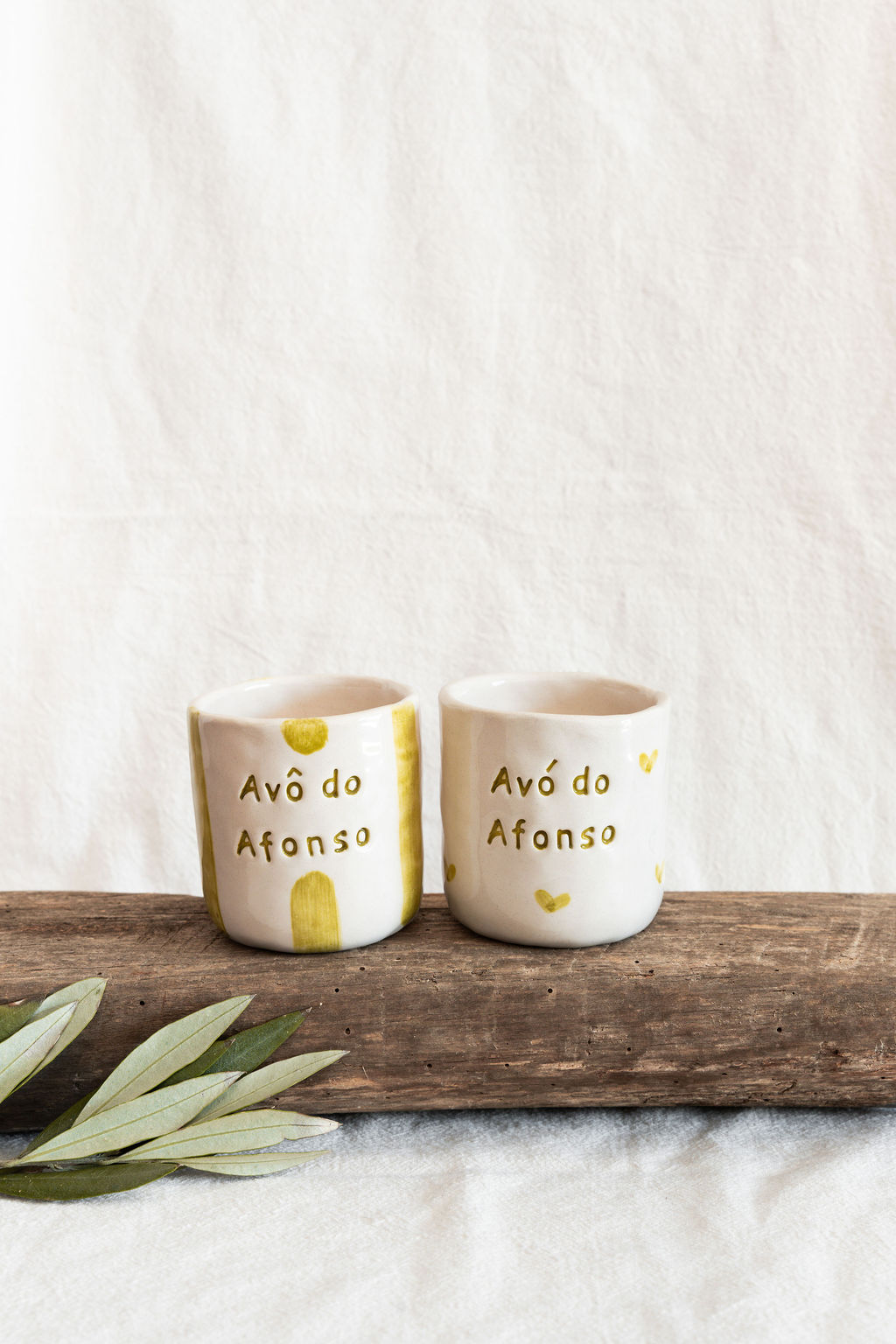 Dois copos de cerâmica brancos com texto e decoração amarela sobre madeira rústica