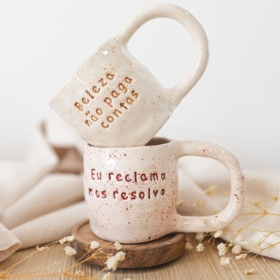 Duas canecas de cerâmica bege com padrões salpicados e frases em português
