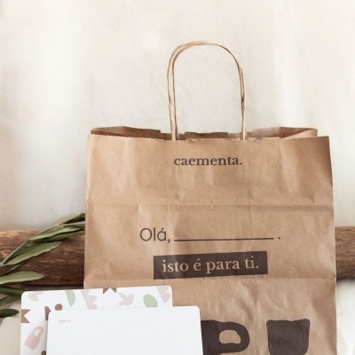 Saco de papel castanho para transporte com texto impresso e dois cartões brancos com folhas verdes