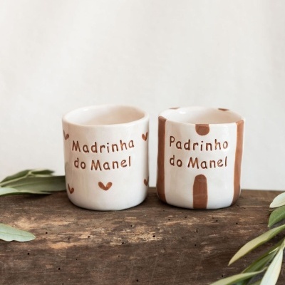 Dois vasos de cerâmica com texto e decoração castanha, sobre tábua de madeira com folhas verdes.