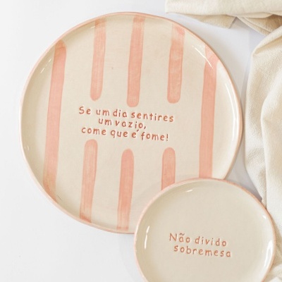 Dois pratos cerâmica bege e rosa com texto em português sobre fundo branco e tecido bege