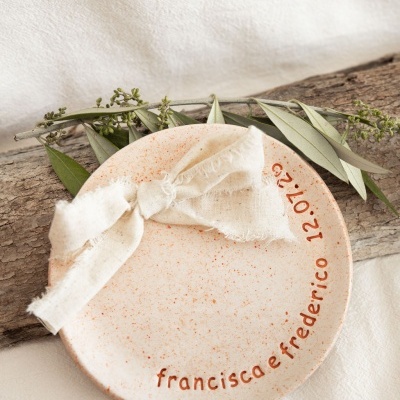 Prato redondo salpicado com fita de tecido cru e folhas verdes sobre madeira.