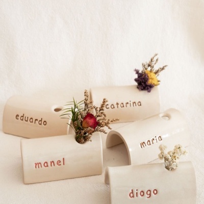 Vasos de cerâmica branca com nomes gravados e flores secas.