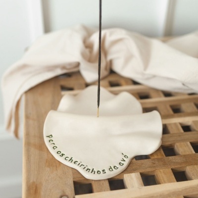 Incensário branco com texto verde e incenso aceso sobre superfície de madeira.