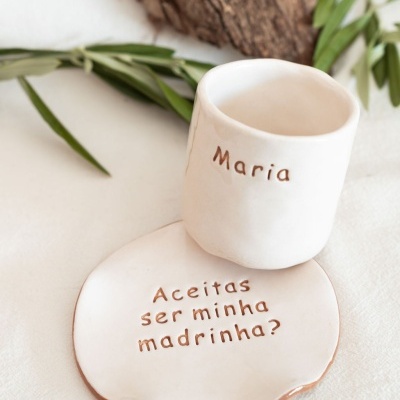 Conjunto cerâmico branco com texto Maria e Aceitas ser minha madrinha? em fundo branco com folhas verdes.
