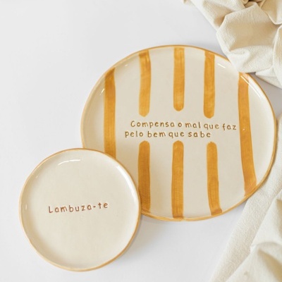 Dois pratos de cerâmica creme com texto em castanho e riscas castanhas, apoiados numa superfície branca junto a tecido bege.