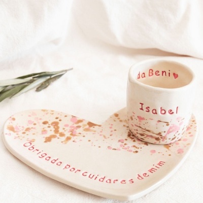 Prato em forma de coração e copo de cerâmica com texto vermelho e manchas coloridas