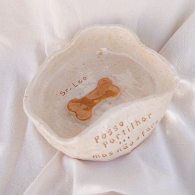 Tigela de cerâmica bege com osso castanho desenhado e texto em português