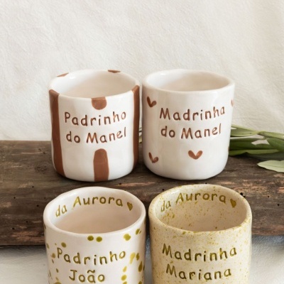 Quatro canecas de cerâmica com textos personalizados e padrões manchados, sobre superfície de madeira.