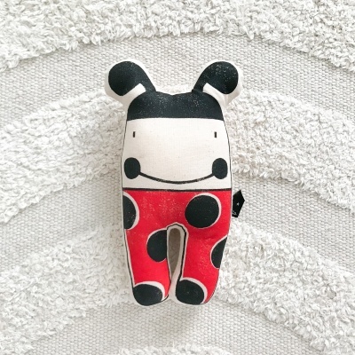 Boneco de peluche colorido com padrões de bolinhas sobre tapete cinza claro