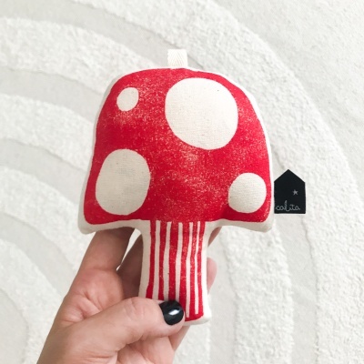 Brinquedo em forma de cogumelo vermelho e branco em fundo claro com padrão ondulado
