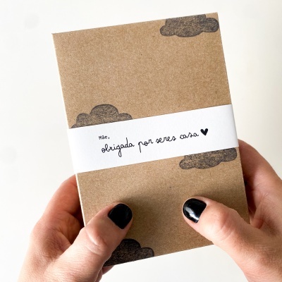 Caderno castanho com nuvens pretas e faixa branca com texto em português