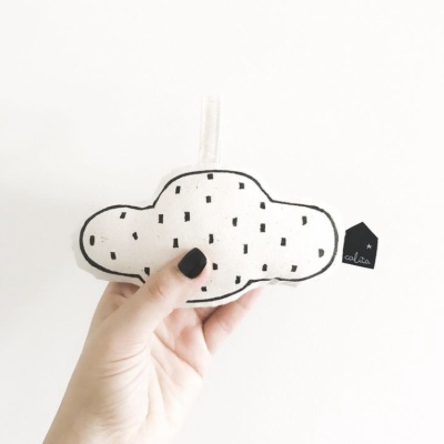 Brinquedo de tecido em forma de nuvem branca com padrões pretos e etiqueta 'colita'