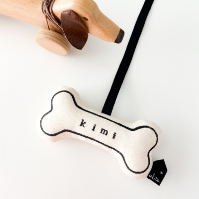 Brinquedo para cão tecido em forma de osso com o nome 'kimi' em preto.