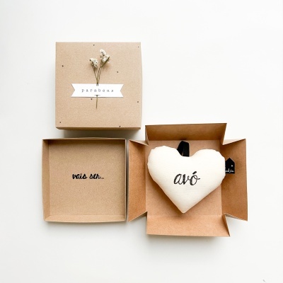 Caixa castanha com tampa decorada com flores secas e palavra 'parabéns' e coração de tecido branco com palavra 'avó' dentro da caixa.