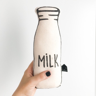 Almofada em formato de garrafa de leite com a palavra MILK em tecido bege e preto