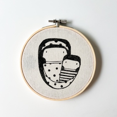 Aro de bordado com tecido bege e ilustração preta simples de dois bonecos.