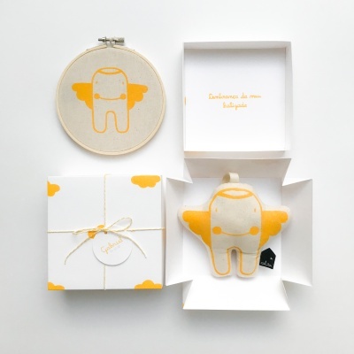 Conjunto com quadro de bordado, boneco de pelúcia amarelo com asas e caixa branca decorada.