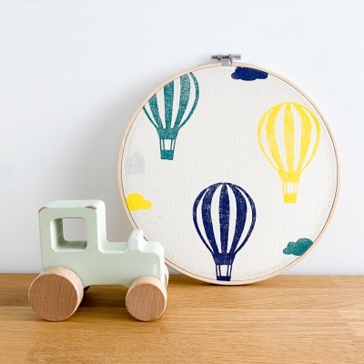 Anel de madeira com tecido e padrão de balões coloridos ao lado de brinquedo de madeira camião