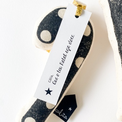 Boneco de tecido preto com bolinhas bege e etiqueta com texto em português