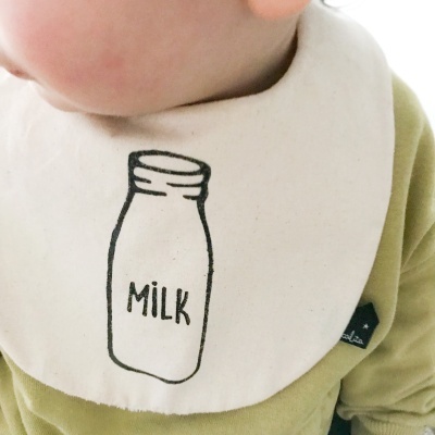 Babete branco com desenho de frasco de leite e texto MILK em preto