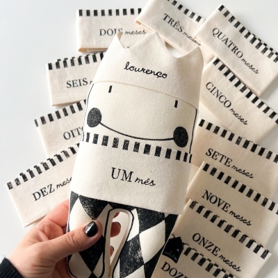 Pelúcia com o nome lourenço e faixas de tecido com meses em português.