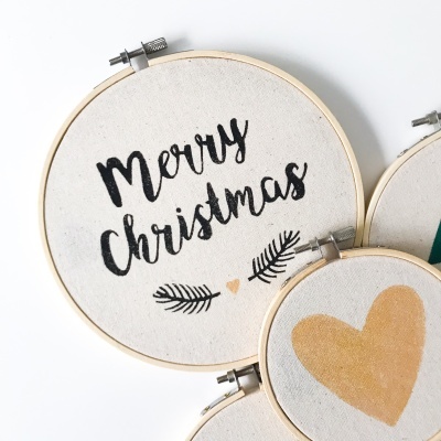 Bordados redondos de tecido claro com texto 'Merry Christmas' e desenhos de ramos e corações em preto e bege