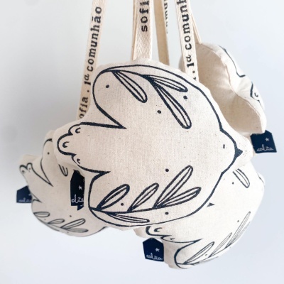 Bonecos de tecido cru em forma de pássaro com desenhos pretos pendurados por fitas brancas com texto.