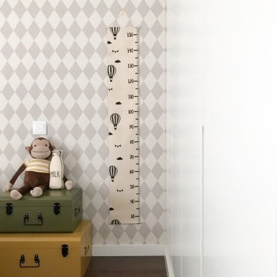 Régua de altura infantil com balões e peluche de macaco sobre malas em quarto com papel de parede losangos cinza