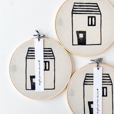 Três bordados redondos com desenho preto de casa e etiquetas brancas penduradas