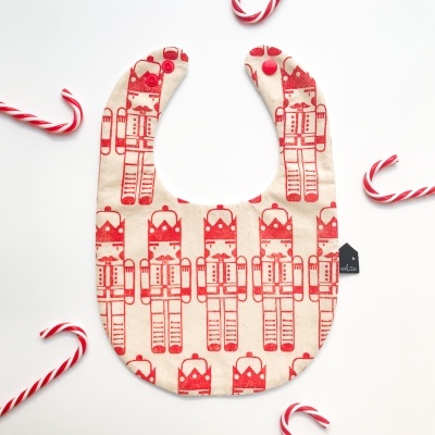 Babete de bebé com padrão de soldados de chumbo vermelhos e creme rodeada por paus de açúcar.