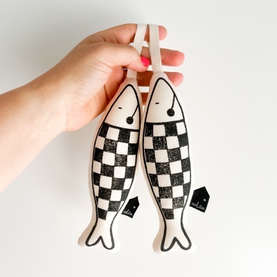 Par de peixes decorativos em tecido branco e preto segurados por uma mão