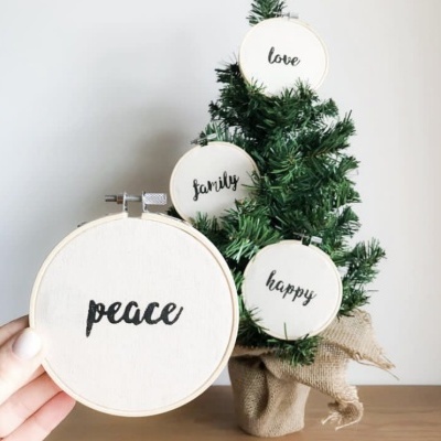 Bordados com palavras em inglês pendurados em árvore de Natal artificial em vaso de juta