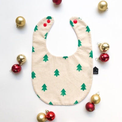 Babete bege com árvores verdes e botões vermelhos, rodeado por bolas douradas e vermelhas de Natal