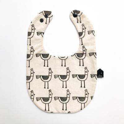 Babete bege com padrão de galinhas pretas e fecho de botão