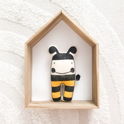 Boneco em tecido com riscas pretas e amarelas dentro de moldura de madeira em forma de casa