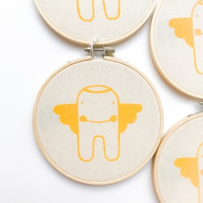 Quadros com tela bege e ilustração amarela de figura com asas e sorriso