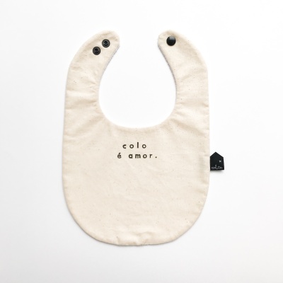 Babete de bebé cru com texto 'colo é amor.' e fechos pretos