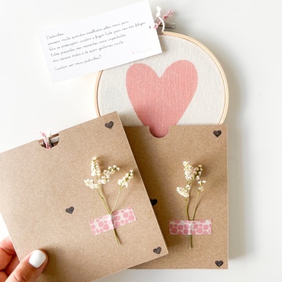 Envelopes de papel castanho com corações, flores secas, bordado com coração cor-de-rosa e cartão com texto manuscrito.