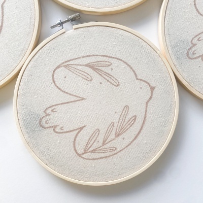 Aros de bordado com desenho de pássaro e elementos florais em tecido bege