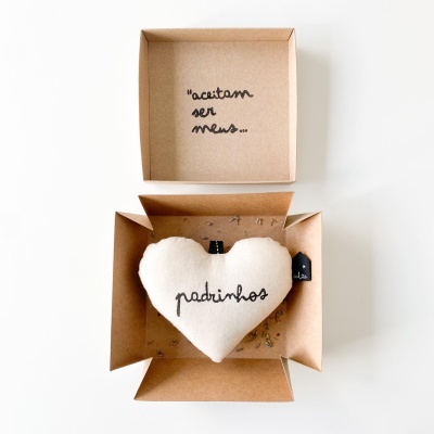 Caixa aberta com almofada coração bege bordada com a palavra padrinhos