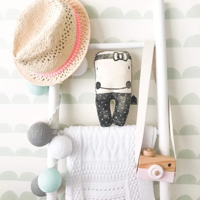 Chapéu de palha com fita rosa, boneco de peluche, candeeiro com bolas coloridas e têxtil branco pendurados numa estrutura branca